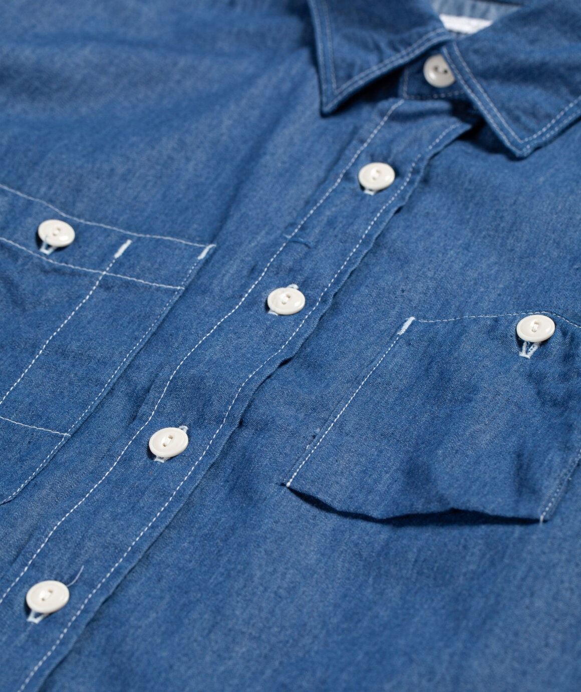 Détail caractéristique des poches asymétriques. Surpiqures contrastées qui collent parfaitement au registre workwear. 