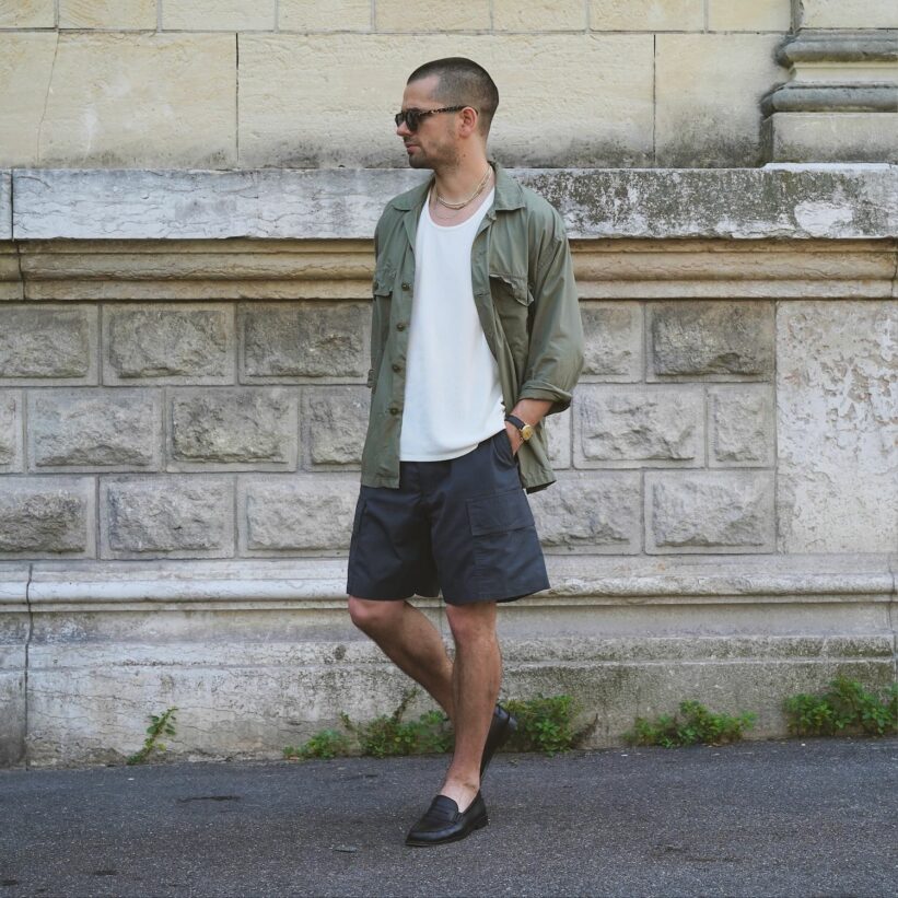 tenue d'été avec une surchemise militaire en popeline de coton tropical, portée avec un débardeur blanc, un short cargo et des mocassins noirs