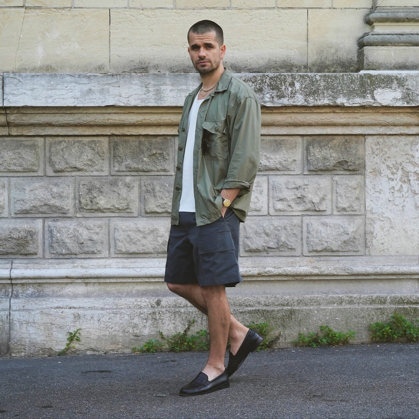 tenue d'été avec une surchemise militaire en popeline de coton tropical, portée avec un débardeur blanc, un short cargo et des mocassins noirs