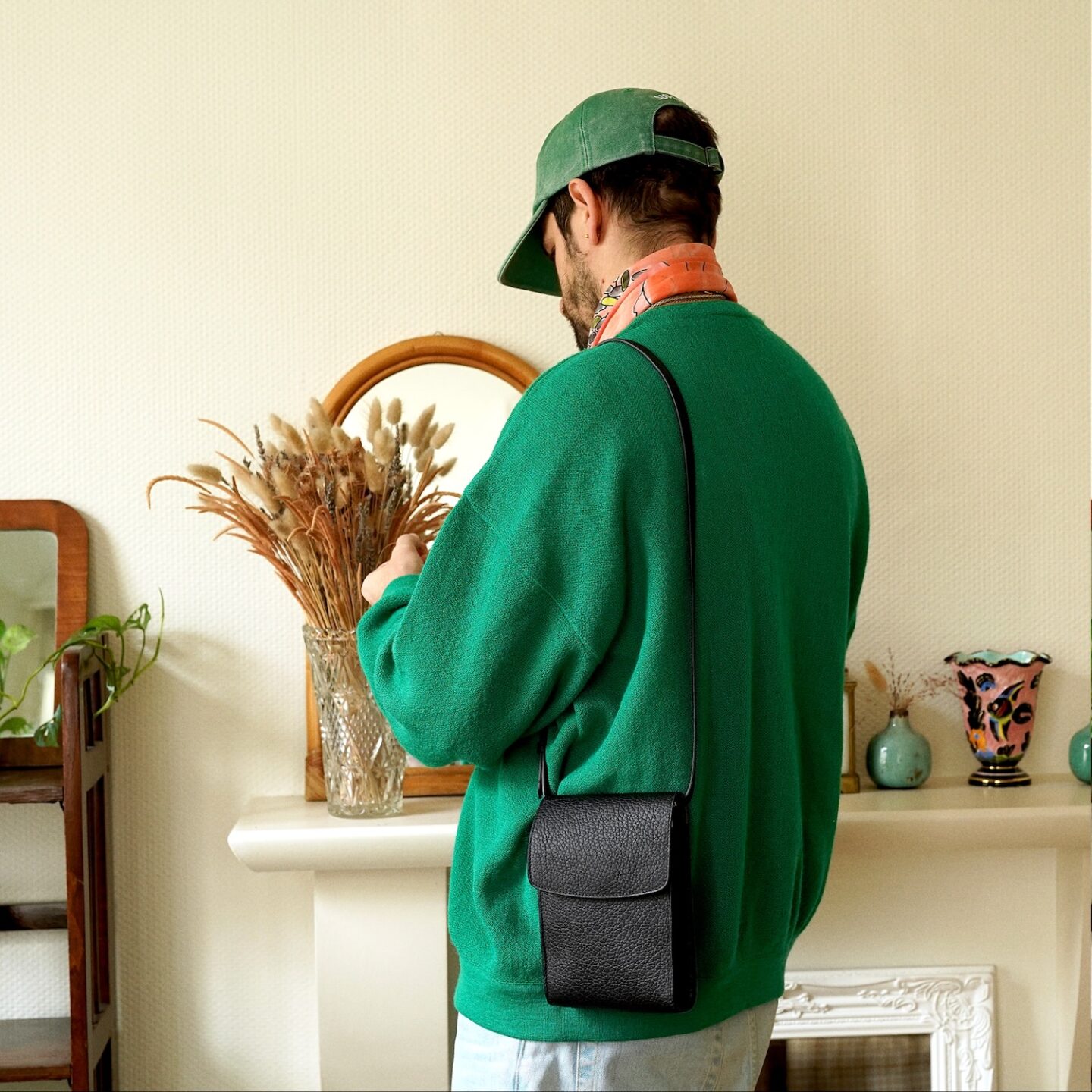 pochette à rabat en cuir grainé noir de la marque de maroquinerie française Laperruque portée dans une tenue avec un cardigan en laine Lacoste vintage, un foulard et une casquette supreme