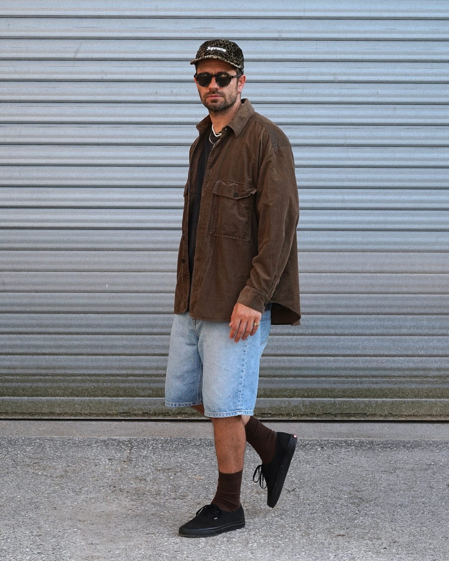surchemise en velours marron de la marque Evan Kinori modèle big shirt, porté avec une casquette supreme léopard et des lunettes arpenteur et un style skate short en denim / vans