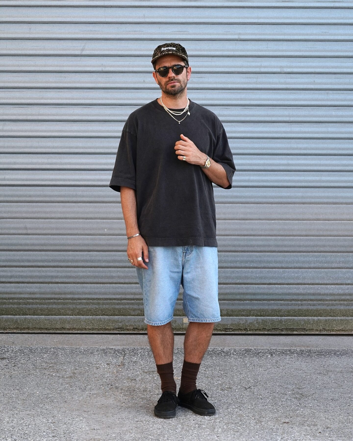 look d'été inspiration skate avec t-shirt oversize drapeau noir, short en denim lee et vans era et supreme velvet leopard camp cap