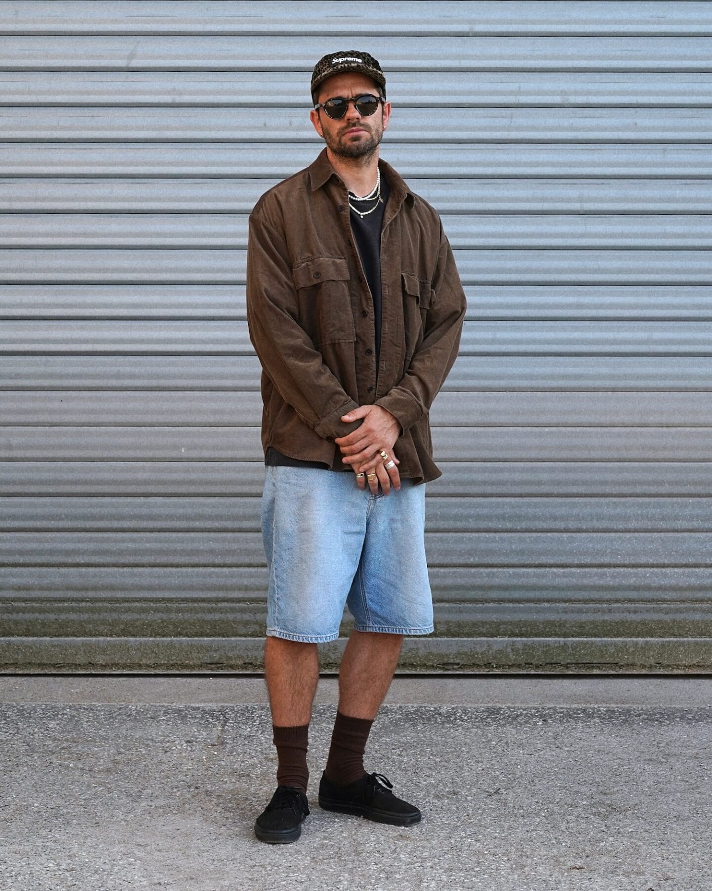 surchemise en velours marron de la marque Evan Kinori modèle big shirt, porté avec une casquette supreme léopard et des lunettes arpenteur et un style skate short en denim / vans